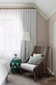 Sessel, Beistelltisch und Stehlampe vor geschlossenem Vorhang in elegantem Schlafzimmer