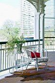 Vase of flowers on side table next to white rattan chair on veranda