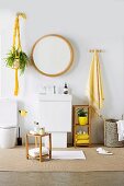 Badezimmer mit rundem Wandspiegel über Waschtisch, davor kleiner Holzschemel, gelbe Farbakzente durch Accessoires