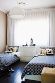 White chest of drawers flanked by twin beds with black and white patterned bedspreads