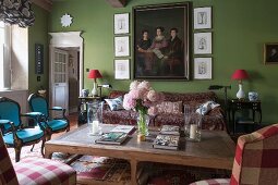 Rustic coffee table and chairs of various styles in green-painted, traditional living room with family portrait on wall