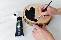 Painting a slice of wood black with a paintbrush