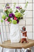 Sommerblumenstrauß in weißer Retro-Porzellanvase auf Holzstuhl mit karibischer Mädchenfigur arrangiert