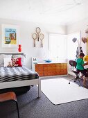 Child's bedroom - boy sitting on chair next to coat rack, bed, sideboard and tennis racquets hung on wall