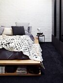 White blanket with pattern of holes on bed with integrated shoe rack on black carpet