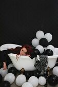 Woman lying exhausted in bathtub filled with balloons