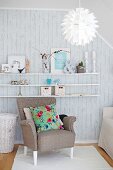 Seating area with shelves of vintage ornaments on exposed concrete wall, armchair with floral scatter cushion and Scandinavian designer lamp
