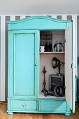 Vintage cupboard painted pastel turquoise with patinated surface; open door showing view of ornaments