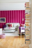 Books stacked on wall-mounted shelves; red and pink striped wallpaper in living room in background