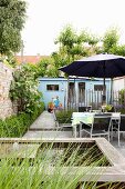 Narrow courtyard garden of terraced house with pond, table, chairs, parasol and shed at far end