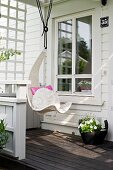 White hanging chair suspended from veranda roof of white wooden house
