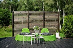 Green wicker easy chairs and set of white side tables on wooden deck in front of wooden screen