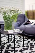 Glass vase of garden flowers on black metal side table and black and white patterned rug