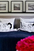 Scatter cushions with comic-style covers on bed with upholstered headboard below framed pictures on wall