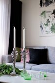 White candles in silver candlesticks and tealight holders on coffee table in front of pale grey sofa