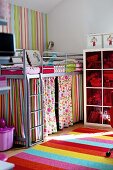 Metal loft bed with colourful curtains in corner of child's bedroom with striped rug