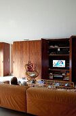 Comfortable, brown leather couch in lounge area; child watching TV, fitted cupboards with rosewood doors and TV behind open door