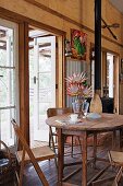 Old wooden furniture and vase of protea in dining area in house with many reclaimed elements