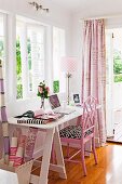 Weisser Schreibtisch mit rosafarbenem Stuhl vor Fenster