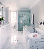 Marble floor tiles, washstand with white base units and glazed shower area in spacious, bright bathroom