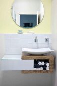Washbasin on wooden shelf base unit with white drawer; round mirror on wall painted pale yellow