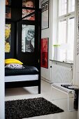 Detail of four-poster bed with black metal frame in front of posters on black wall in traditional interior