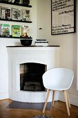 Classic-style, white shell chair with wooden frame next to open fireplace in rustic interior
