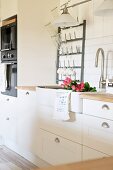 Ausschnitt einer weissen Landhausküche, Rosen in Spülbecken, an Wand Metall Flaschentrockner