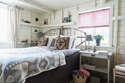 Folkloristische Tagesdecke auf Doppelbett mit Kopfteil in weißem, holzverkleidetem Schlafzimmer