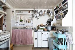 Retro tea trolley below shelves on wall and sink unit next to cooker in rustic kitchen