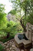 Betonbrunnen an Natursteinmauer im Waldähnlichen Garten