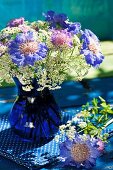 Cobalt blue glass vase of violet scabious and cow parsley on blue fabric with white polka dots