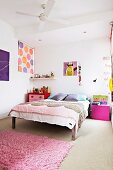Bett mit Tagesdecke, mit pinkfarbenen Nachtschränkchen und rosafarbenem Flokati in freundlichem Kinderzimmer