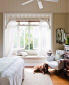 Dog in front of armchair in bedroom; romantic bay window with curtains and integrated window seat