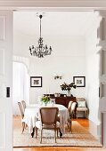 Dining area with antique chairs and large, oval table below chandelier; bay window in background