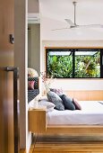 View through open door of stacked pillows on floating modern bed and palm trees seen through open window