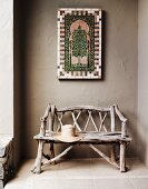 Rustikale Sitzbank aus Ästen, an grau geschlämmter Wand marokkanisches Mosaikbild in der Loggia