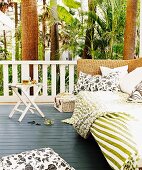 Cushions and blankets on wicker daybed in relaxation area on veranda in tropical surroundings