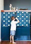 Boy opening door of blue-painted cabinet with graphic pattern
