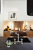 Undermount sink with vintage tap fittings in dark worksurface and illuminated gas stove in background