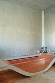 Bathtub made from curved concrete slab and glass side wall with red mosaic tiles inside in minimalist bathroom