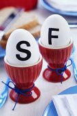 Eggs with stick-on initials in red eggcups on breakfast table
