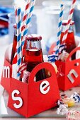 Bottles of soft drinks, napkins, drinking straws and sweets in small red paper bags decorated with letters