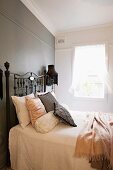 Französisches Bett mit antikem Metall Gestell vor grau getönter Wand in schlichtem Schlafzimmer mit nostalgischem Vintage-Flair