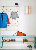 Coat rack with neon orange accents, fuse box covered in fabric and bench spray-painted blue