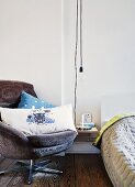DIY bedside table lit by simple light bulb between bed with Danish designer bedspread and cord velvet armchair with tiger scatter cushion