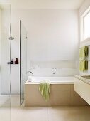 Pale bathroom with niche above bathtub and floating washstand; floor-level shower behind glass screen to one side