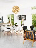 Open-plan interior in Australian beach house with 60s retro armchairs, classic shell chairs in dining area and concrete breakfast bar; black and white portraits of children