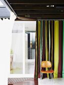 Rooms forming a right angle around corner of courtyard with encircling boardwalk and mosquito curtains; classic Eames chair (LCM) against striped curtain
