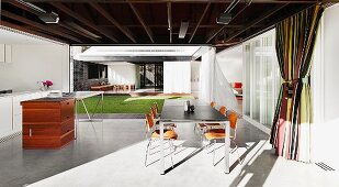 View from purist, modern kitchen-dining room with classic chairs through completely open facades into central, encircled courtyard with lawn